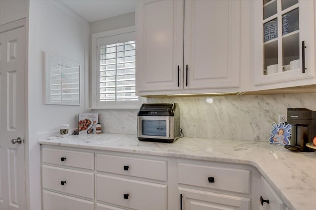 kitchen with light stone counters, tasteful backsplash, glass insert cabinets, and white cabinets