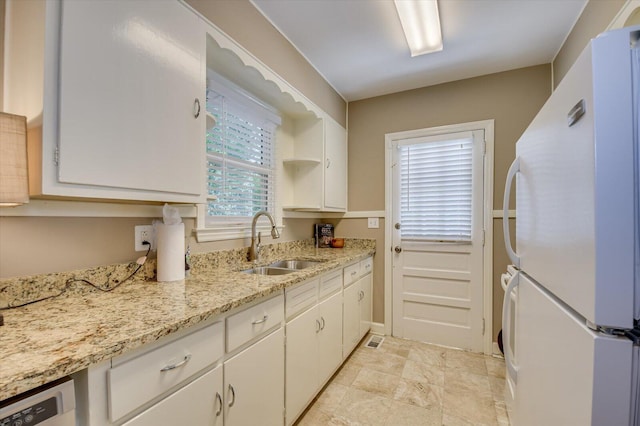 kitchen with white cabinets, dishwashing machine, light stone counters, freestanding refrigerator, and a sink