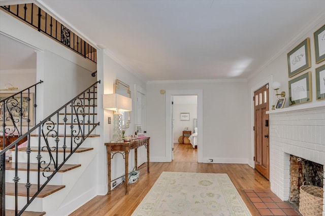 foyer featuring baseboards, wood finished floors, stairs, crown molding, and a brick fireplace