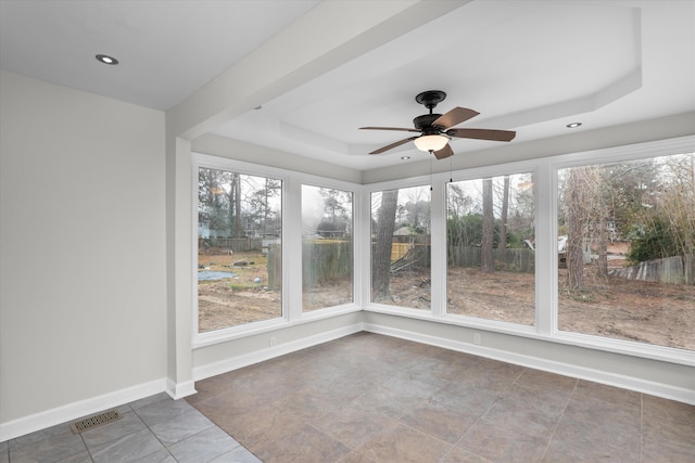 unfurnished sunroom featuring ceiling fan, a tray ceiling, and a wealth of natural light