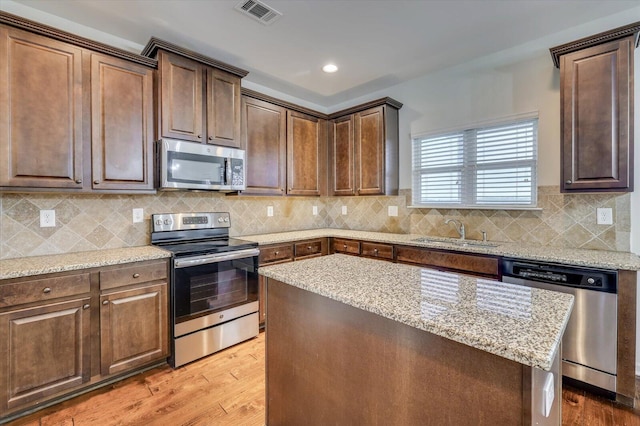 kitchen featuring backsplash, sink, light hardwood / wood-style flooring, light stone countertops, and appliances with stainless steel finishes