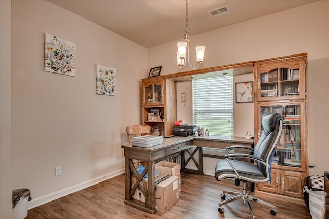 home office with wood-type flooring and an inviting chandelier