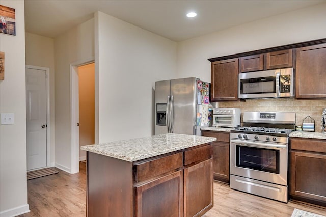 kitchen featuring decorative backsplash, appliances with stainless steel finishes, light wood-type flooring, dark brown cabinetry, and a kitchen island