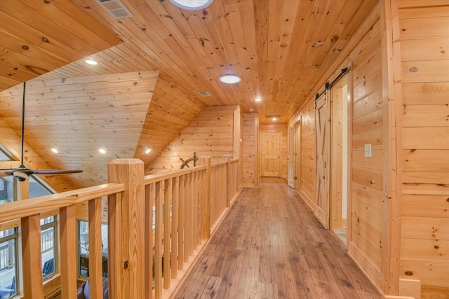 corridor with wood walls, a barn door, wooden ceiling, and wood-type flooring