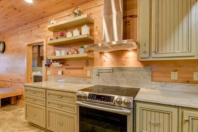 kitchen with light stone countertops, stainless steel range with electric stovetop, wall chimney exhaust hood, and wood walls