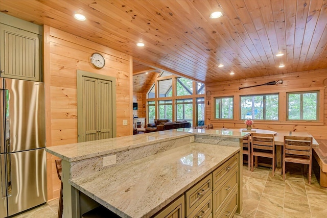 kitchen with stainless steel fridge, light stone counters, wood ceiling, wooden walls, and a center island