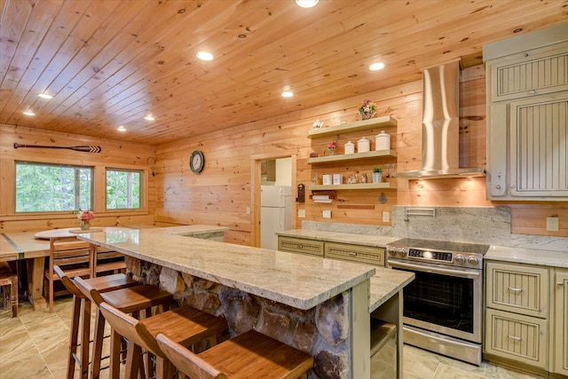 kitchen featuring stainless steel electric range, wood walls, white refrigerator, island range hood, and light stone counters