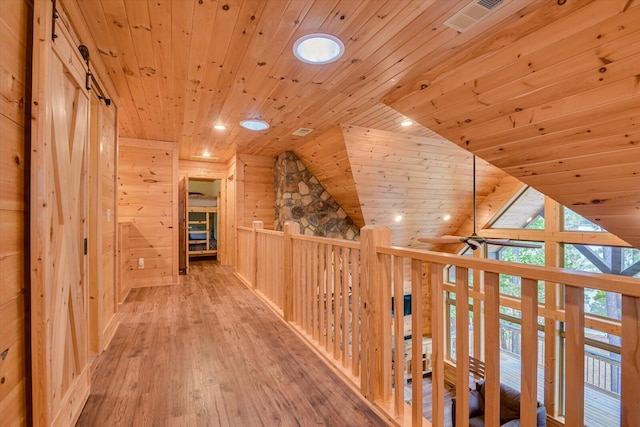 corridor featuring wooden walls, wood ceiling, lofted ceiling, and light hardwood / wood-style floors