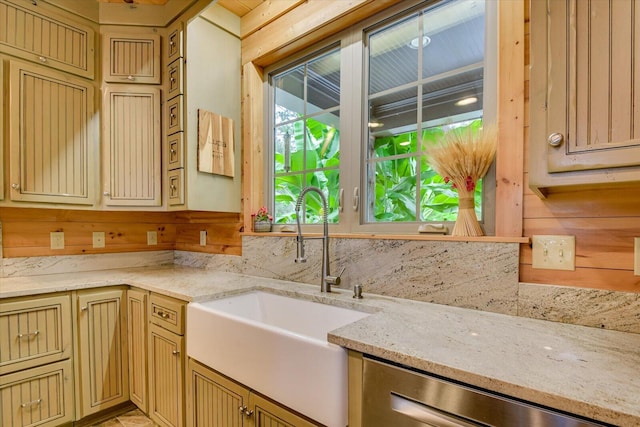 kitchen featuring stainless steel dishwasher, light stone countertops, sink, and wooden walls