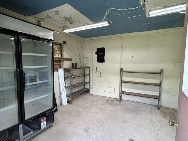 basement featuring concrete block wall and fridge