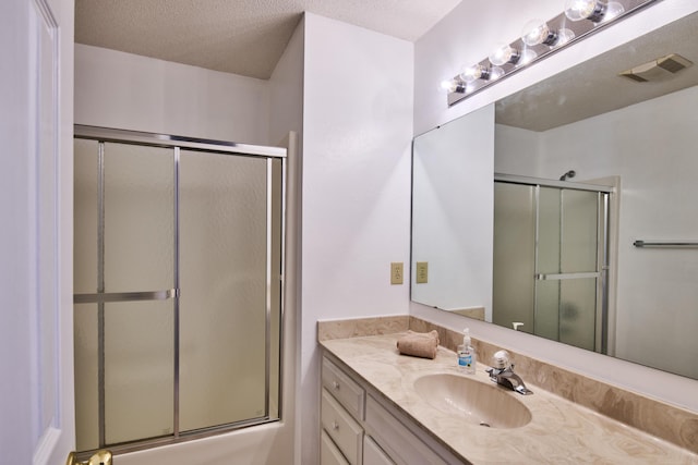 full bathroom with visible vents, a textured ceiling, vanity, and bath / shower combo with glass door