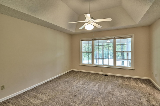 unfurnished room with a ceiling fan, a raised ceiling, dark carpet, and baseboards