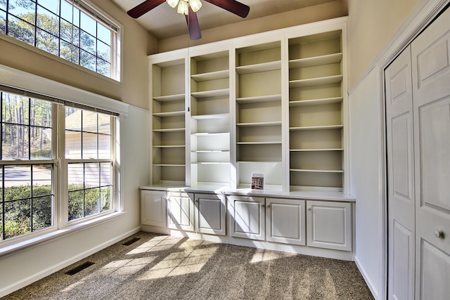 unfurnished office featuring ceiling fan, dark colored carpet, visible vents, and baseboards