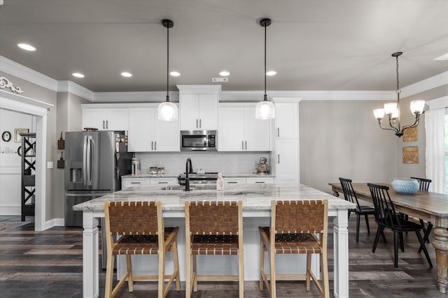 kitchen featuring stainless steel appliances, white cabinetry, a center island with sink, and decorative light fixtures