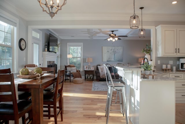 dining room with light wood-type flooring, ceiling fan with notable chandelier, and ornamental molding