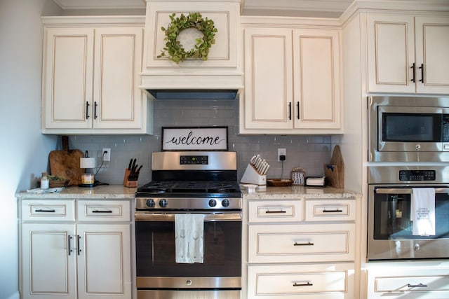 kitchen with exhaust hood, decorative backsplash, light stone countertops, stainless steel appliances, and cream cabinetry