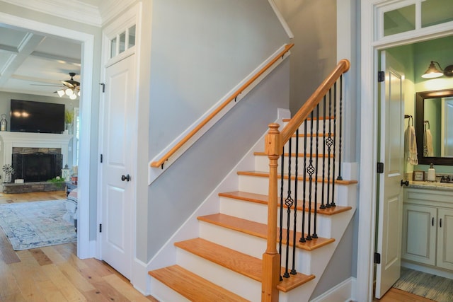 stairway featuring coffered ceiling, ceiling fan, a fireplace, wood-type flooring, and beamed ceiling