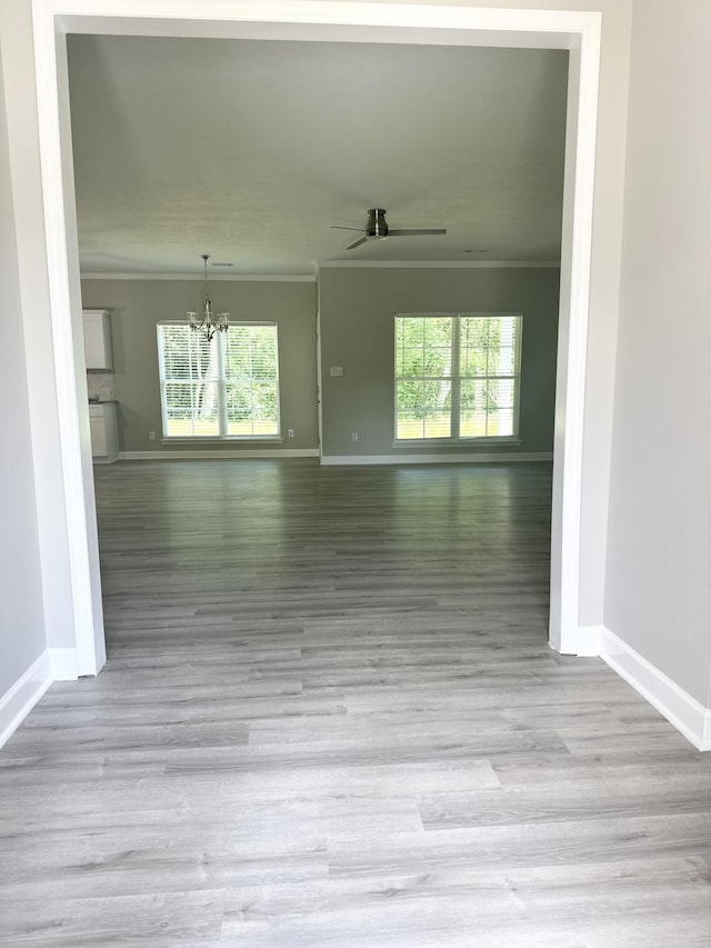 unfurnished room featuring light wood-type flooring, ceiling fan with notable chandelier, and ornamental molding