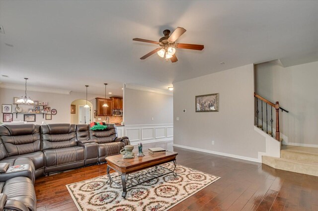 living room featuring dark wood-type flooring, ceiling fan with notable chandelier, and ornamental molding