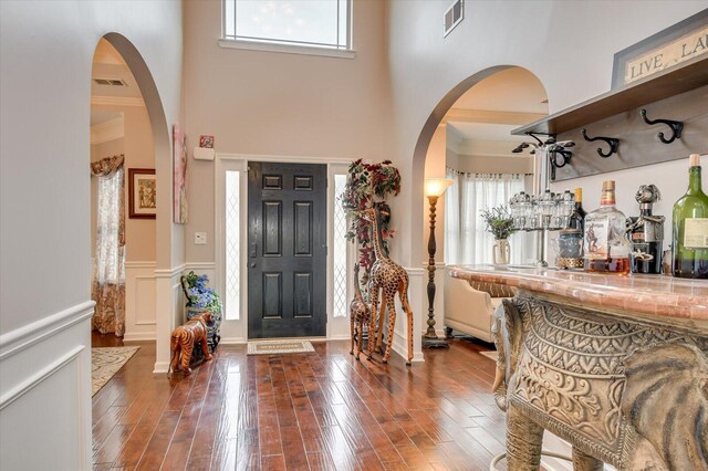 entrance foyer with ornamental molding, bar, and dark wood-type flooring