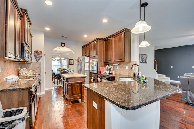 kitchen with sink, a center island, stainless steel appliances, dark stone countertops, and pendant lighting