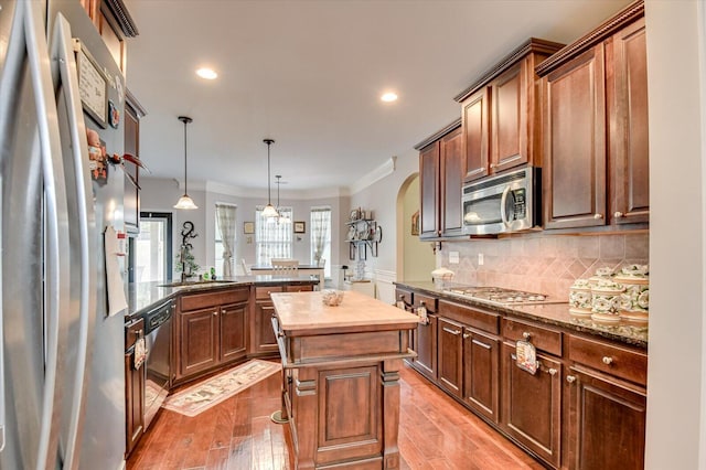 kitchen featuring a center island, crown molding, light hardwood / wood-style floors, decorative light fixtures, and appliances with stainless steel finishes