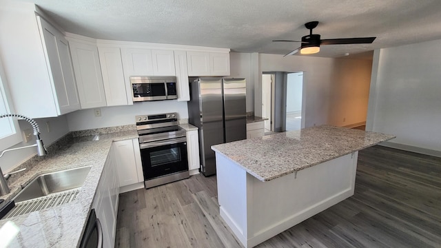 kitchen featuring white cabinets, a kitchen island, wood finished floors, stainless steel appliances, and a sink