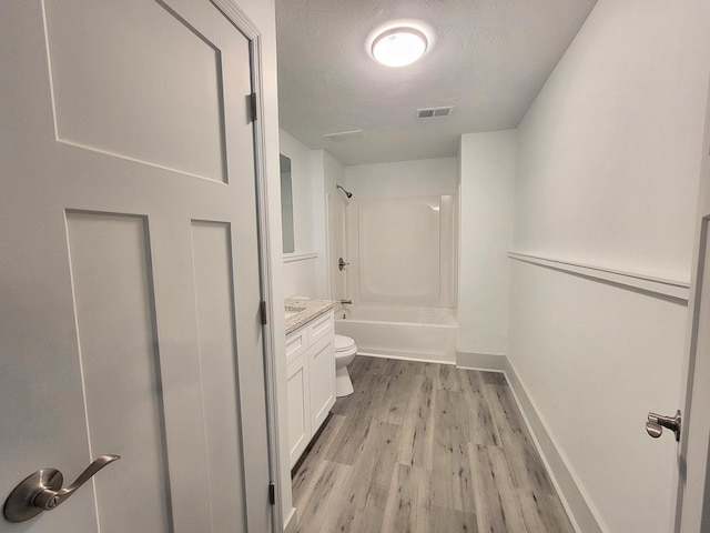 hallway featuring a textured ceiling, light wood-type flooring, visible vents, and baseboards