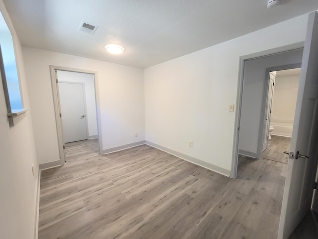 empty room with light wood-type flooring, visible vents, and baseboards