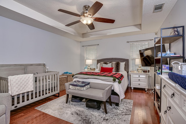 bedroom with dark hardwood / wood-style flooring, a textured ceiling, a tray ceiling, and ceiling fan