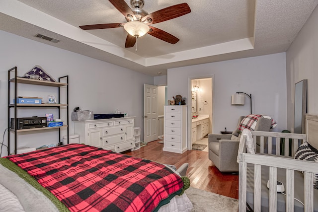 bedroom featuring ceiling fan, a raised ceiling, light hardwood / wood-style flooring, ensuite bathroom, and a textured ceiling