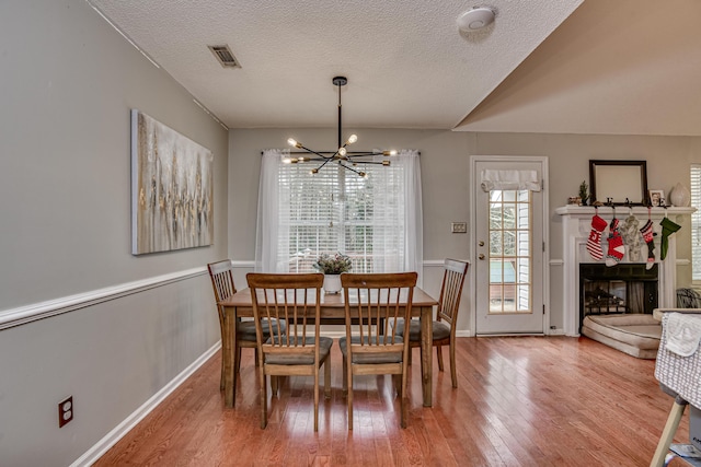 dining space featuring wood-type flooring, a textured ceiling, an inviting chandelier, and vaulted ceiling