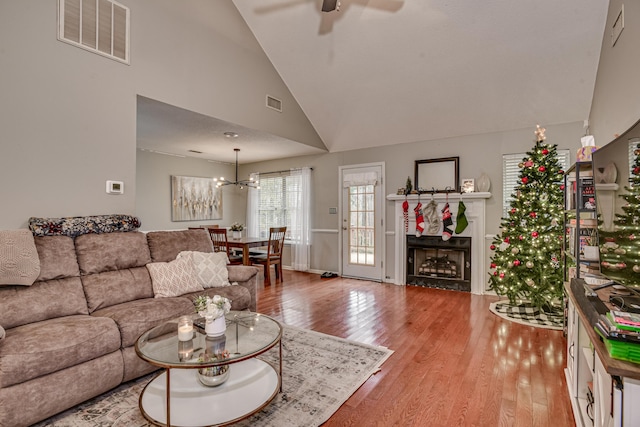 living room with high vaulted ceiling, ceiling fan with notable chandelier, and light wood-type flooring