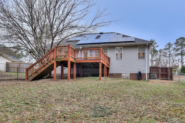 rear view of house featuring central AC unit, solar panels, a deck, and a yard