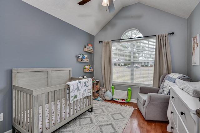 bedroom with a crib, hardwood / wood-style floors, vaulted ceiling, and ceiling fan