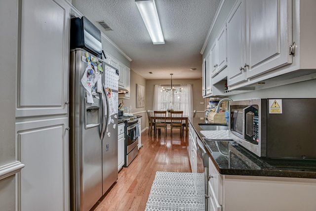 kitchen with white cabinetry, sink, an inviting chandelier, pendant lighting, and appliances with stainless steel finishes