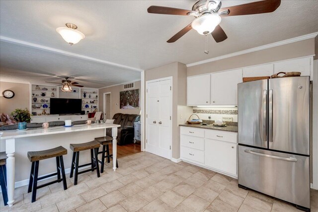 kitchen featuring a kitchen breakfast bar, built in shelves, a textured ceiling, white cabinetry, and stainless steel refrigerator