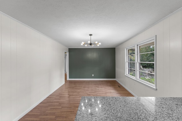 unfurnished dining area featuring hardwood / wood-style flooring, a notable chandelier, a textured ceiling, and wooden walls