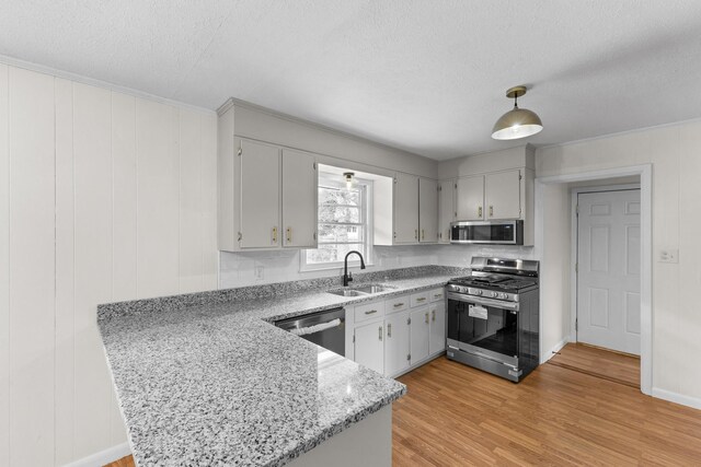 kitchen with sink, a textured ceiling, light hardwood / wood-style floors, kitchen peninsula, and stainless steel appliances