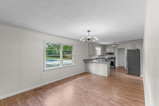 kitchen featuring sink, light hardwood / wood-style flooring, appliances with stainless steel finishes, kitchen peninsula, and a chandelier