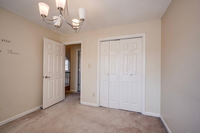 unfurnished bedroom with a textured ceiling, light colored carpet, baseboards, a closet, and an inviting chandelier