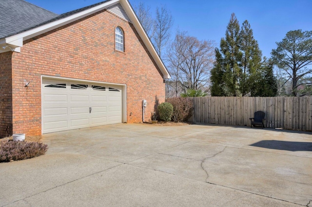 view of side of home featuring concrete driveway, brick siding, and fence