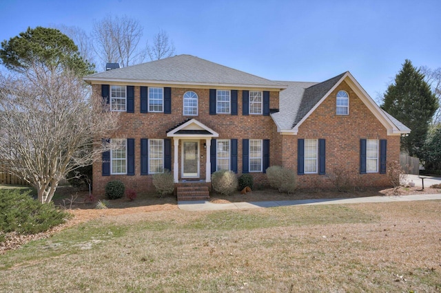 view of front of house featuring brick siding, a chimney, and a front lawn