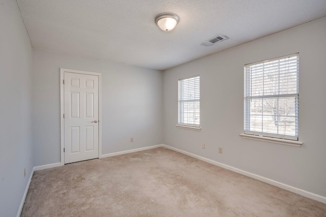 unfurnished room featuring visible vents, light carpet, a textured ceiling, and baseboards