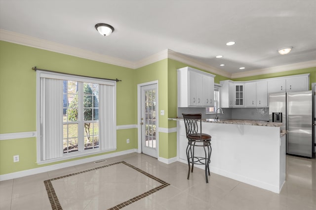 kitchen with kitchen peninsula, tasteful backsplash, white cabinets, stainless steel fridge with ice dispenser, and crown molding