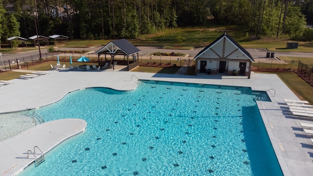 pool featuring fence, a gazebo, an outbuilding, a patio area, and a forest view