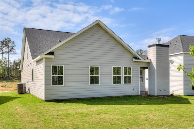 back of house with a yard, a shingled roof, cooling unit, and a chimney