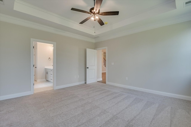 unfurnished bedroom featuring crown molding, baseboards, light colored carpet, a raised ceiling, and ensuite bath