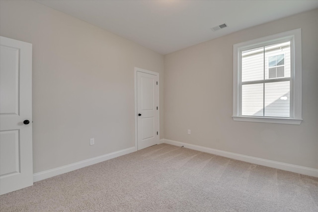 empty room with baseboards, light colored carpet, and visible vents