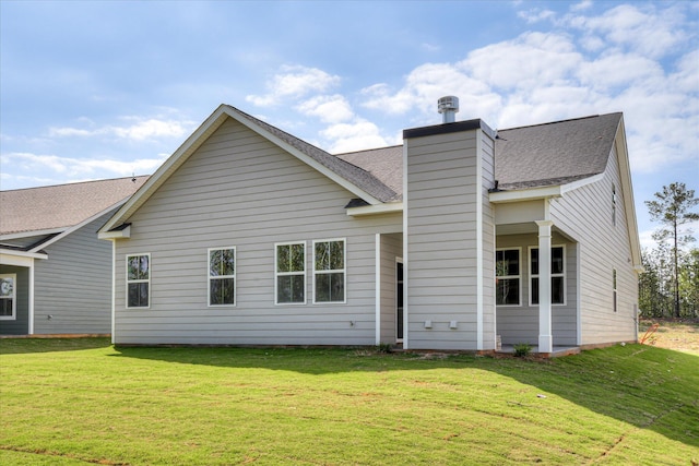 rear view of property with roof with shingles, a yard, and a chimney